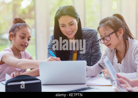 Female teacher and girl students researching at laptop in library Stock Photo
