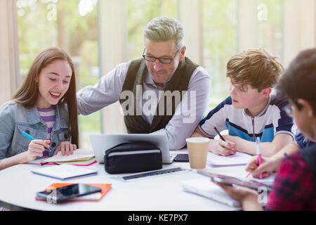 Male teacher and students researching at laptop in library Stock Photo