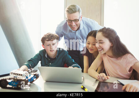 Smiling male teacher and students programming robotics at laptop in classroom Stock Photo