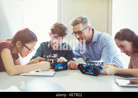 Male teacher helping students assembling robotics in classroom Stock Photo