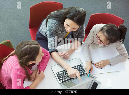 Female teacher helping girl students researching at laptop at library table Stock Photo