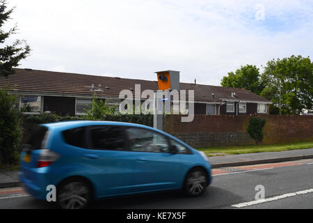 A blue small car passes a yellow fixed speed camera on a residential road with houses in the background. Stock Photo