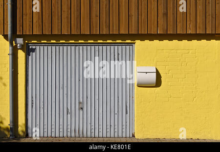 Yellow brick wall with garage door, mail box, downspout and brown wooden paneling on the second floor
