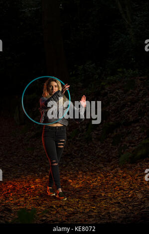 Girl looks directly into the camera through a hoop, which she holds in front of her, other arm with palm facing out, and creative lighting in woods, copy space above. Stock Photo