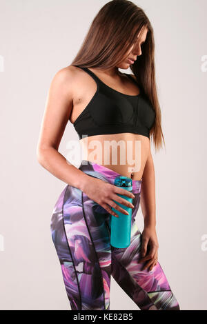 Young girl, holding a water blue bottle, dressed in leggings ant sports bra, isolated against a white background. Stock Photo