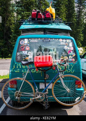 A camper van in a parking lot covered with bumper stickers and graffiti, and with a luggage on a rack and bike on the back; Field, Alberta, Canada Stock Photo