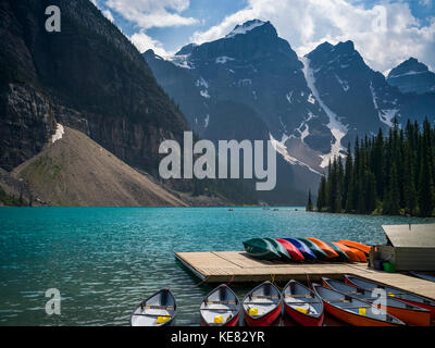 Canoes in the water and sitting on a dock along the shore of Moraine Lake in the Canadian Rocky Mountains; Eldon, Alberta, Canada Stock Photo