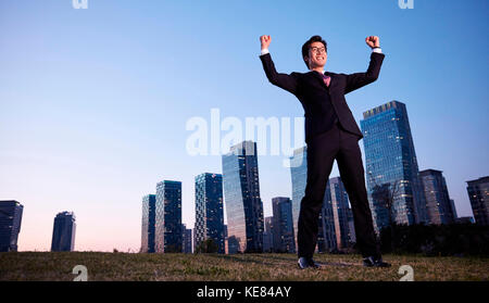Businessman standing raising his hands against skyscrapers in city at sunset Stock Photo