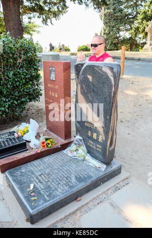 A visitor posing at Bruce Lee and Brandon Lee Tomb Stones in Lakeview Cemetery in Seattle Stock Photo