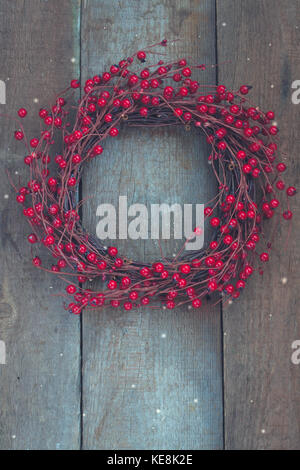 Christmas wreath with red berries on the old wooden background. Toned. Snowflakes. Stock Photo