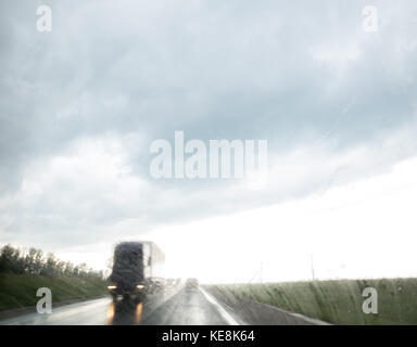 View through moving truck windscreen at oncoming trucks and cars. Rainy day. Rainy drops on the windscreen. Stock Photo