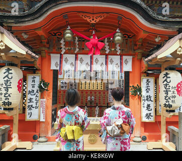 Rear view of two girls wearing kimonos making a wish at the Jishu-jinja inner shrine located within the Kiyomizu-dera temple in Kyoto Japan Stock Photo
