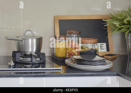 Stainless steel pot and pasta jars on black granite top counter Stock Photo
