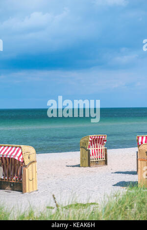 Red striped roofed chairs on empty sandy beach in Travemunde. Grass bush in foreground. Germany Stock Photo