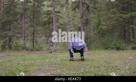 A young athletic man jumping, performs strength exercises, a crossfit element. In pine forest, summer Stock Photo