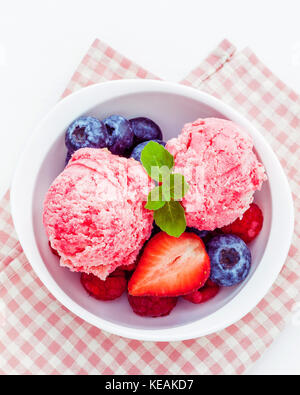 Close Up ice cream mixed berry fruits raspberry ,blueberry ,strawberry and peppermint leaves setup in white bowl on white wooden background . Summer a Stock Photo