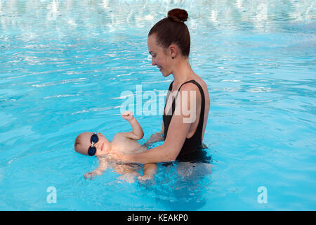Woman teaching baby to swim in pool Stock Photo