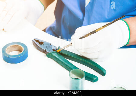 Close-up of a female confectioner in blue uniform and white gloves paints tassel pliers from dairy Belgian chocolate, on a white table is an insulatin Stock Photo