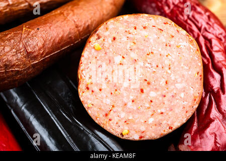 Piece of delicious smoked sausage resting on other sausages in the background. Open sliced surface show spices and meat. Stock Photo