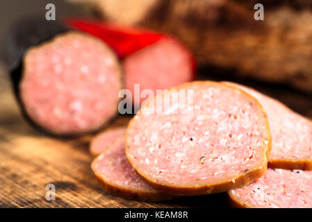 Closeup of delicious smoked sausage sliced on a burnt wooden cutting board. Shallow focus on front slice. Sausages blurred in background. Stock Photo