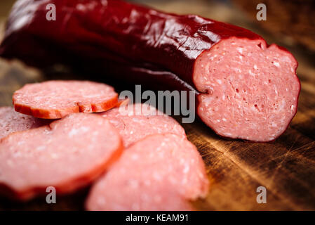 Handmade delicious smoked sausage on burnt wooden cutting board with pile of slices. Stock Photo