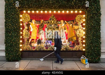 A cleaner at work outside a Christmas window display, themed as With Love From, which is a celebration of the cities Selfridges calls home, at Sefridges department store in Oxford Street, London. Stock Photo