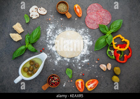 Raw dough for homemade pizza with with ingredients and herbs  flat lay on dark stone background. Stock Photo