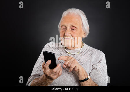 Senior Woman Using Smartphone Over Grey Background Stock Photo