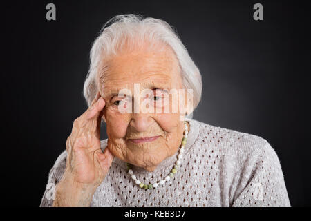 Portrait Of Thoughtful Senior Woman Over Grey Background Stock Photo