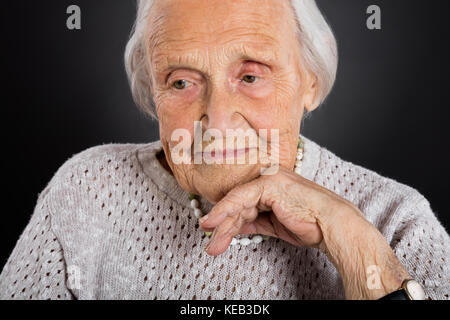 Portrait Of Thoughtful Senior Woman Over Grey Background Stock Photo
