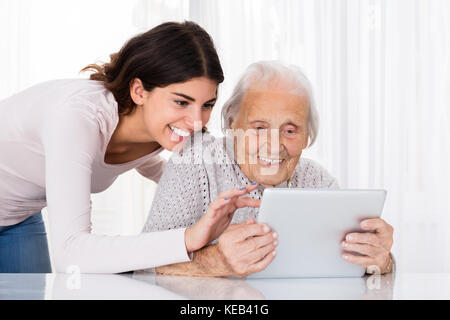 Young Woman Helping Her Grandmother For Using A Digital Tablet On Desk At Home Stock Photo