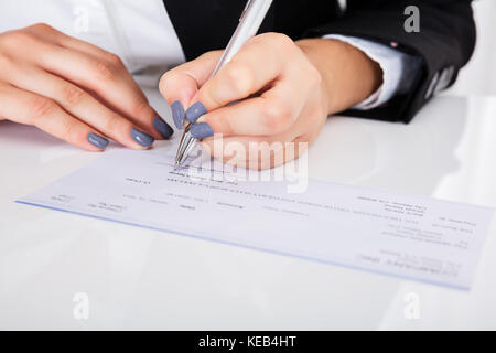 Close-up Of Person's Hand Signing Cheque On Desk Stock Photo