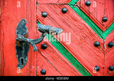 Old vintage and rusted door handle installed on an old red and green weathered and cracked grunge wooden door. Stock Photo