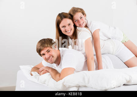 Happy Family Lying On Top Of Each Other In Their Bedroom Stock Photo