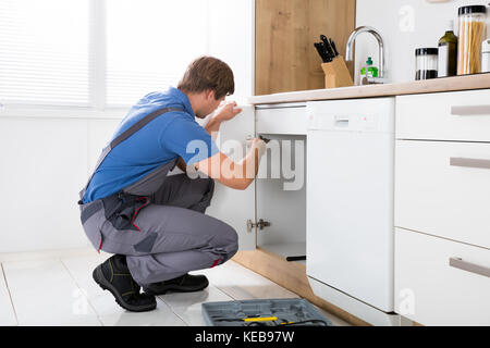 Repairman In Overalls Repairing Cabinet Hinge In Kitchen Stock Photo