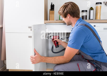 Side View Of Young Male Handyman Fixing Cabinet Using Wireless Screwdriver Stock Photo