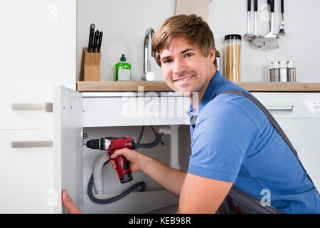 Side View Of Young Male Handyman Fixing Cabinet Using Wireless Screwdriver Stock Photo