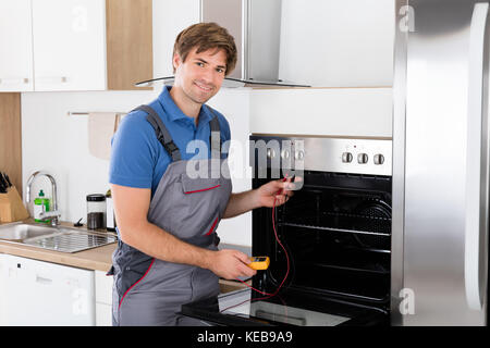Young Male Technician Checking Oven With Digital Multimeter Stock Photo