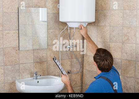 Young Male Plumber Holding Clipboard Checking Electric Boiler In Bathroom Stock Photo