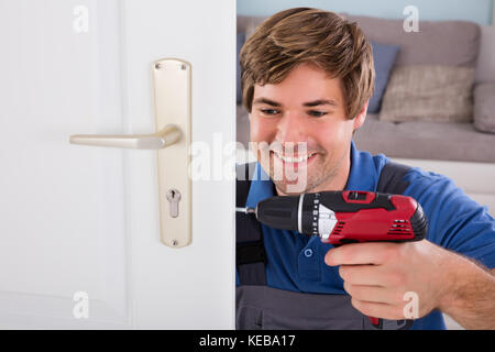 Smiling Young Carpenter Install Door Lock Using Wireless Screwdriver At Home Stock Photo
