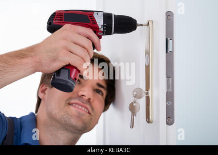 Close-up Of Smiling Happy Young Male Installing Door Lock On Door Using Wireless Screwdriver Stock Photo