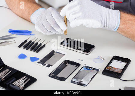 Close-up Of Person's Hand Wearing Glove Repairing Cellphone Using Screwdriver Stock Photo