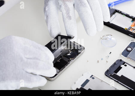 Close-up Of Person's Hand Wearing Glove Repairing Cellphone Using Screwdriver Stock Photo