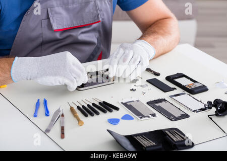 Close-up Of Person's Hand Wearing Glove Repairing Cellphone Using Screwdriver Stock Photo