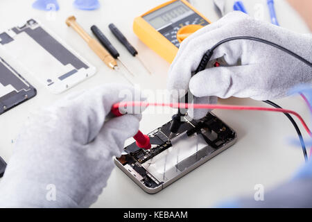 High Angle View Of Person Checking Damaged Mobile Phone With Digital Multimeter Stock Photo