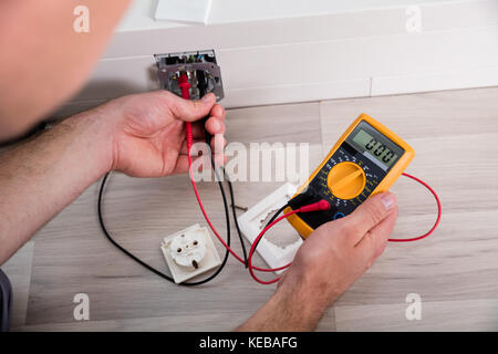 Close-up Of Person's Hand Holding Multimeter Checking Socket Voltage In A Wall Fixture Stock Photo