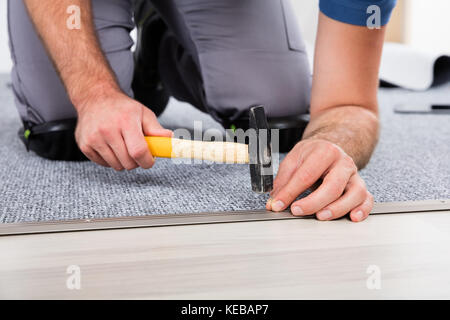 Close-up Of Person's Hand Using Hammer And Nail For Fixing Carpet Stock Photo