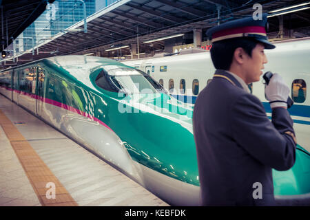 On Japan Railways both the trains and the service are polished. A shinkansen leaves Tokyo Station with a guard in the foreground. Stock Photo