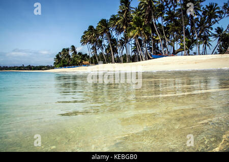 Saud beach view with selective focus on transparent sea looking at undeveloped palm fringed and idyllic tropical paradise. Perfect travel destination Stock Photo