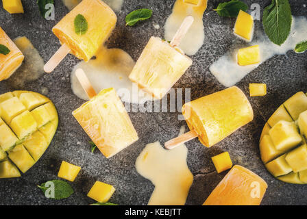 Ice cream, popsicles. Organic dietary foods, desserts. Frozen mango smoothie, with mint leaves and fresh mango fruit, on black stone table. Copy space Stock Photo